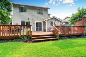 Back yard house exterior with spacious wooden deck with patio area and attached pergola. 