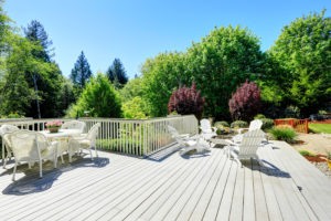 Beautiful backyard deck with white wicker table set fire pit and chairs.