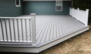 New composite deck on the back of a house with green vinyl siding with white railings.